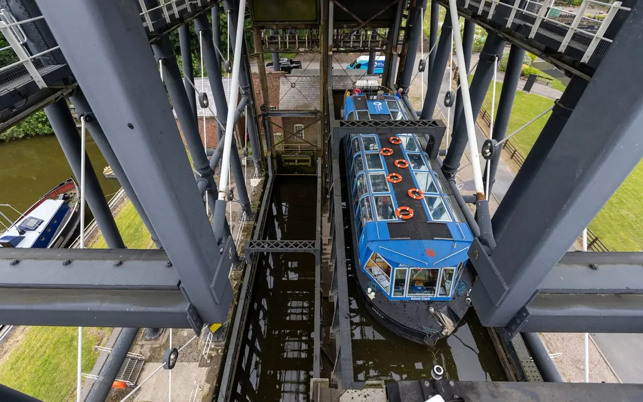 Two blue passenger boats moored in a boat lock with metal gates and structural supports visible overhead.