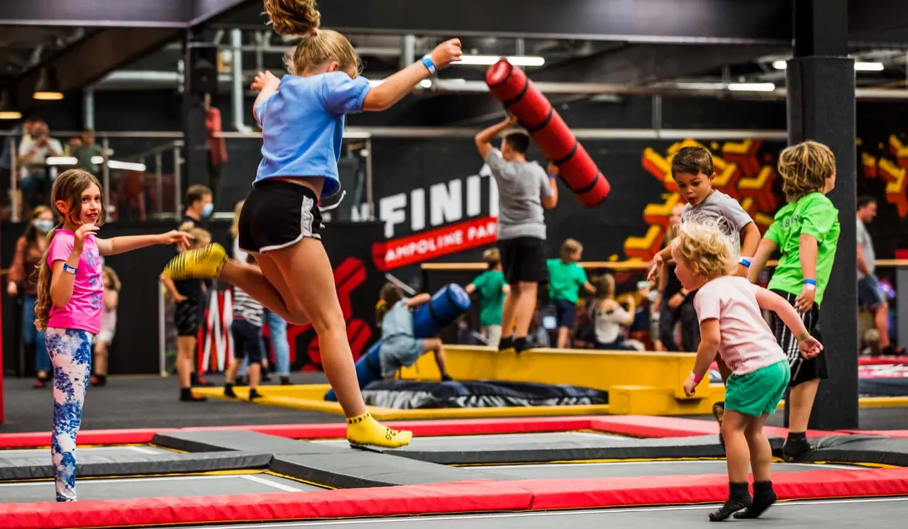 Children jumping and playing on padded trampolines at an indoor trampoline park.