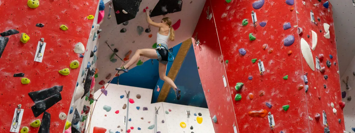Young person rock climbing on a high indoor climbing wall with coloured holds.