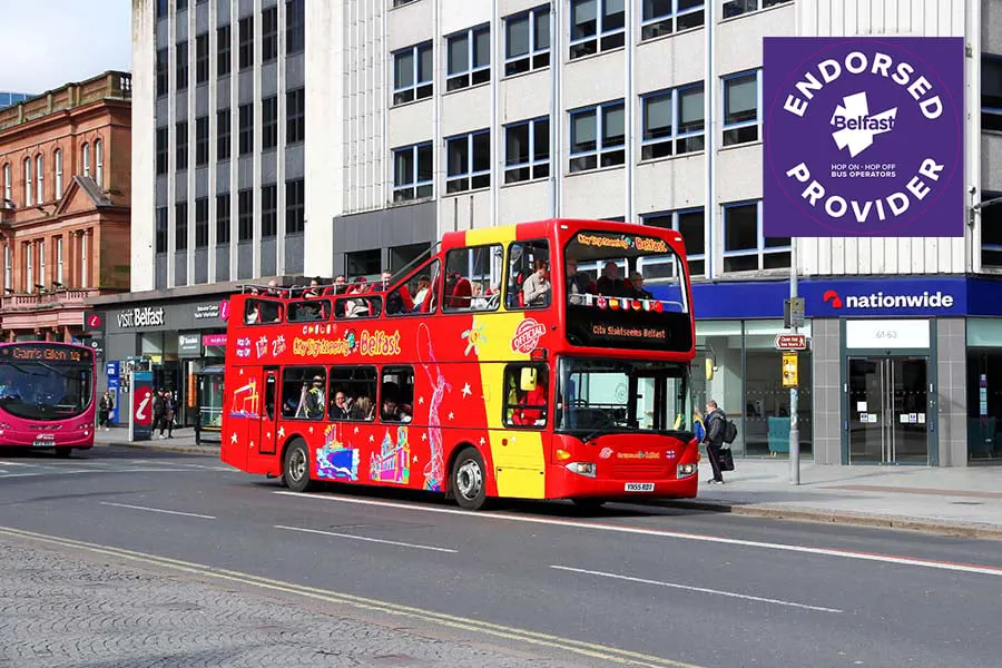 A red and yellow open-top double-decker tour bus on a city street with modern office buildings behind it.