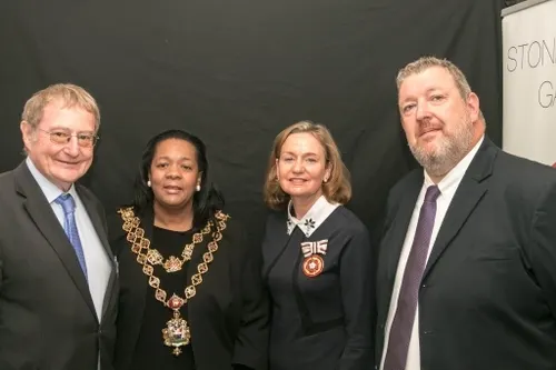 Four adults in formal business attire standing together against a dark backdrop at an indoor event.