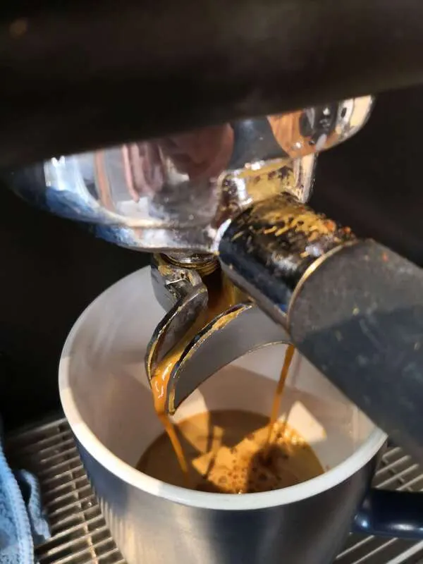 Espresso pouring from a coffee machine into a white cup.