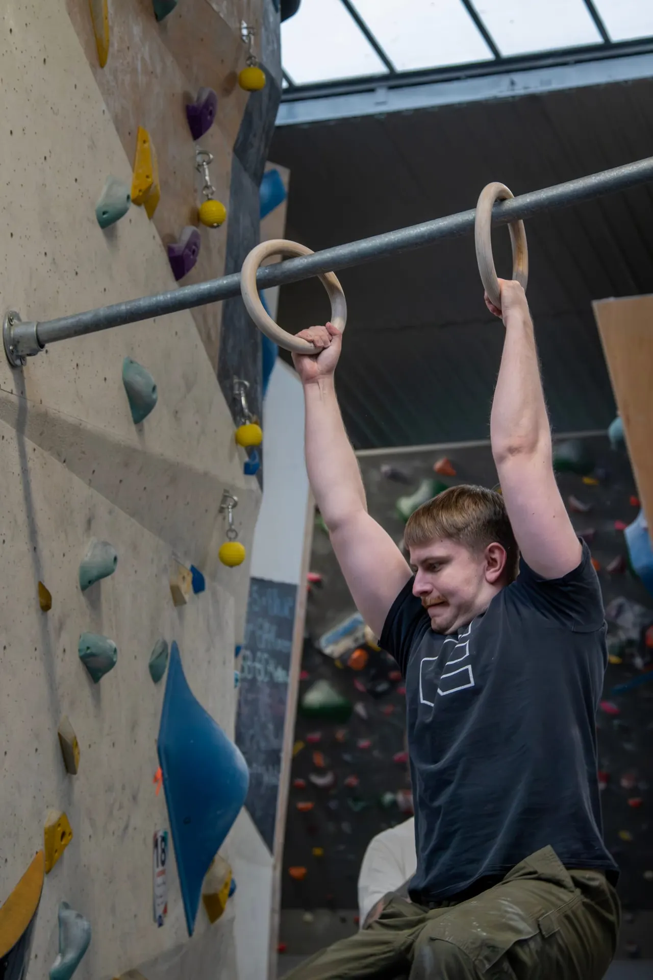 Young person using wooden rings on a climbing wall with coloured holds during an indoor climbing session.