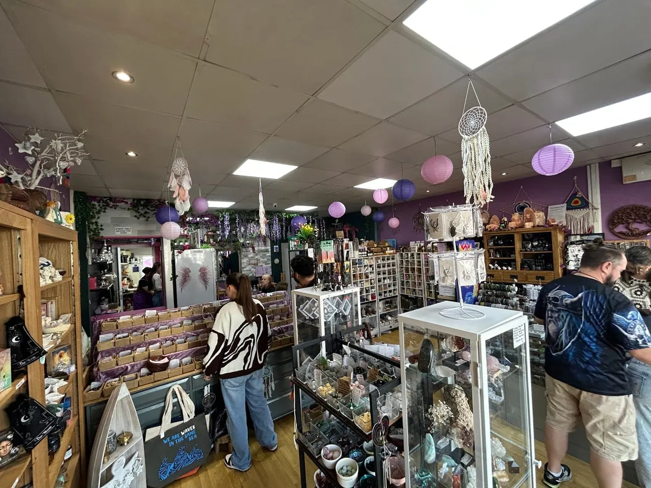 Customers browsing inside a spirituality and wellness shop with purple walls, decorated with dreamcatchers and hanging lanterns.