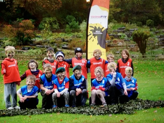 Group of children in red and blue sportswear posing together outdoors in a garden setting.