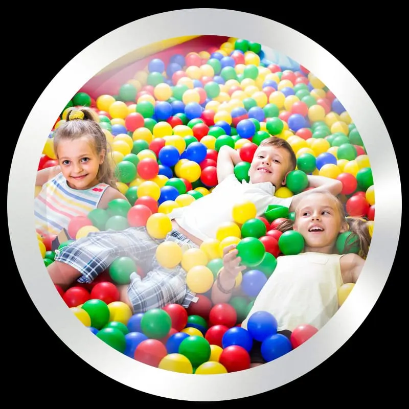 Three children playing and smiling in a ball pit filled with colourful plastic balls.