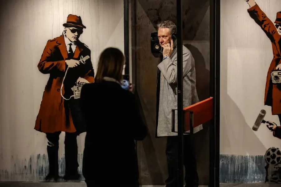 Visitor photographs vintage spy-themed street art murals featuring characters in retro clothing and period details on display walls.