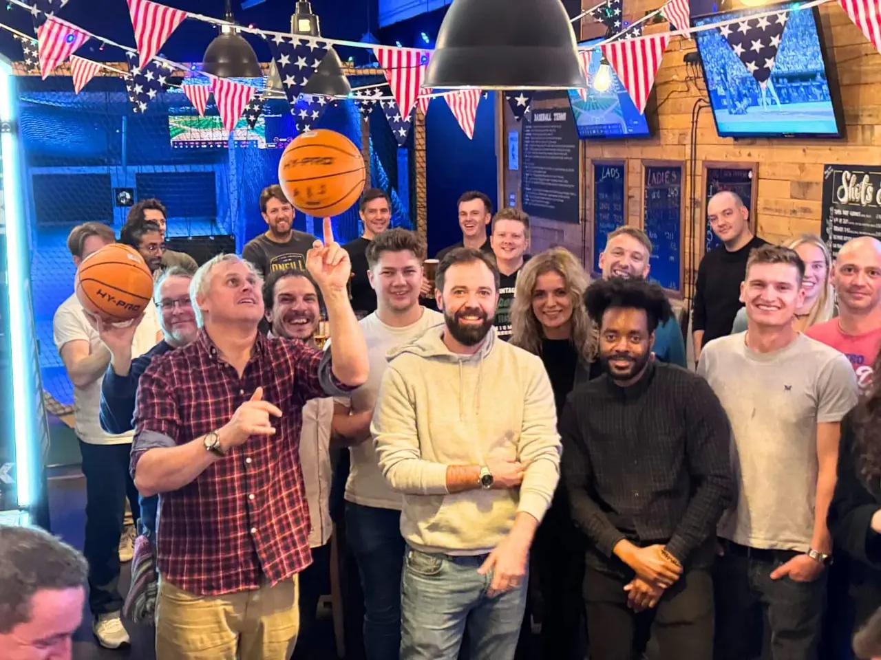Large group of people indoors playing with basketballs at a sports bar decorated with American bunting and flags.