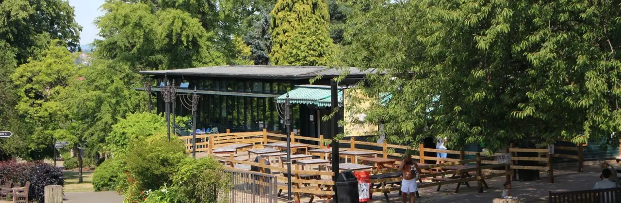 Outdoor café with wooden seating area surrounded by mature trees in a park setting.