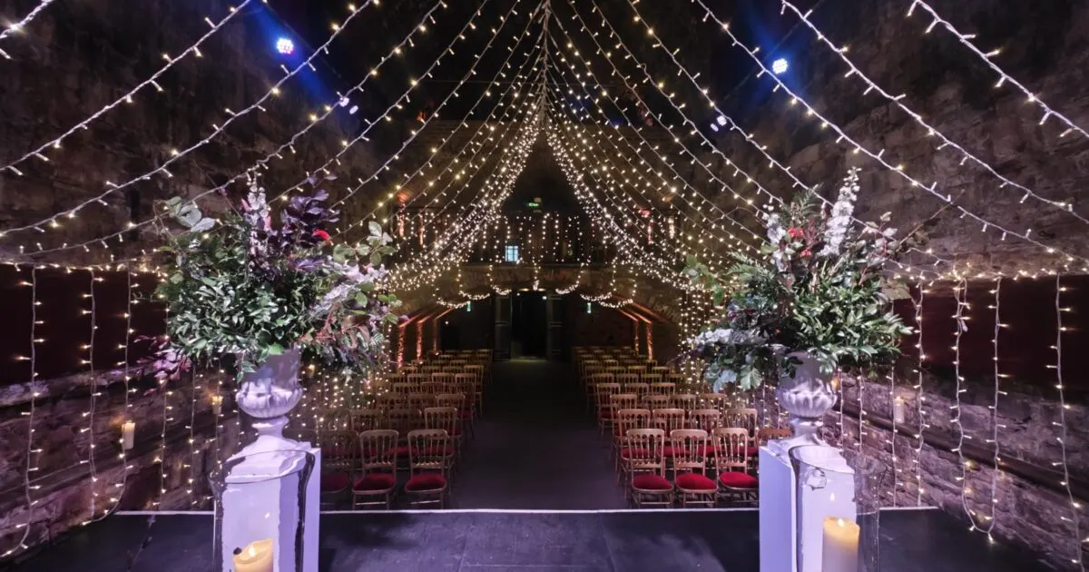 Illuminated wedding ceremony venue with rows of chairs flanking a central aisle decorated with floral arrangements and strung with thousands of fairy lights.