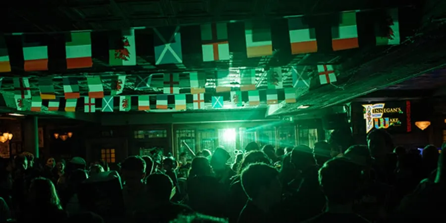 Crowded nightclub interior with green lighting and geometric flag decorations overhead.