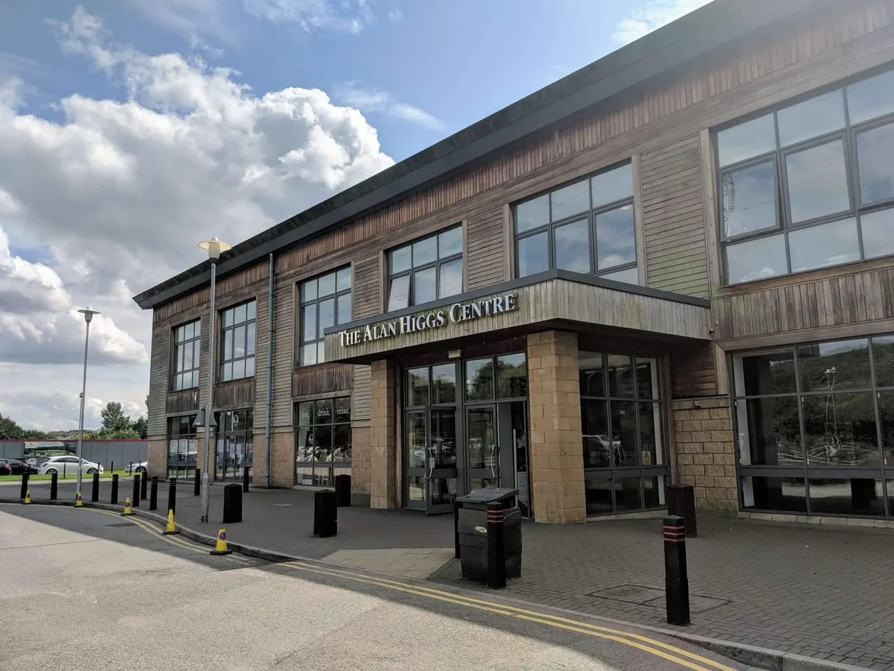 Modern leisure centre building with wooden cladding and large windows under blue sky with white clouds.