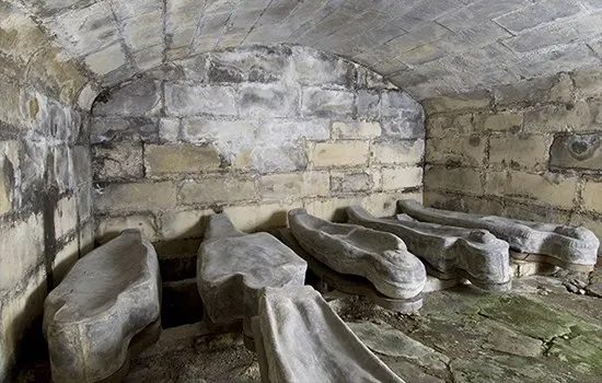 Stone coffins arranged on the floor inside a vaulted medieval castle chamber.