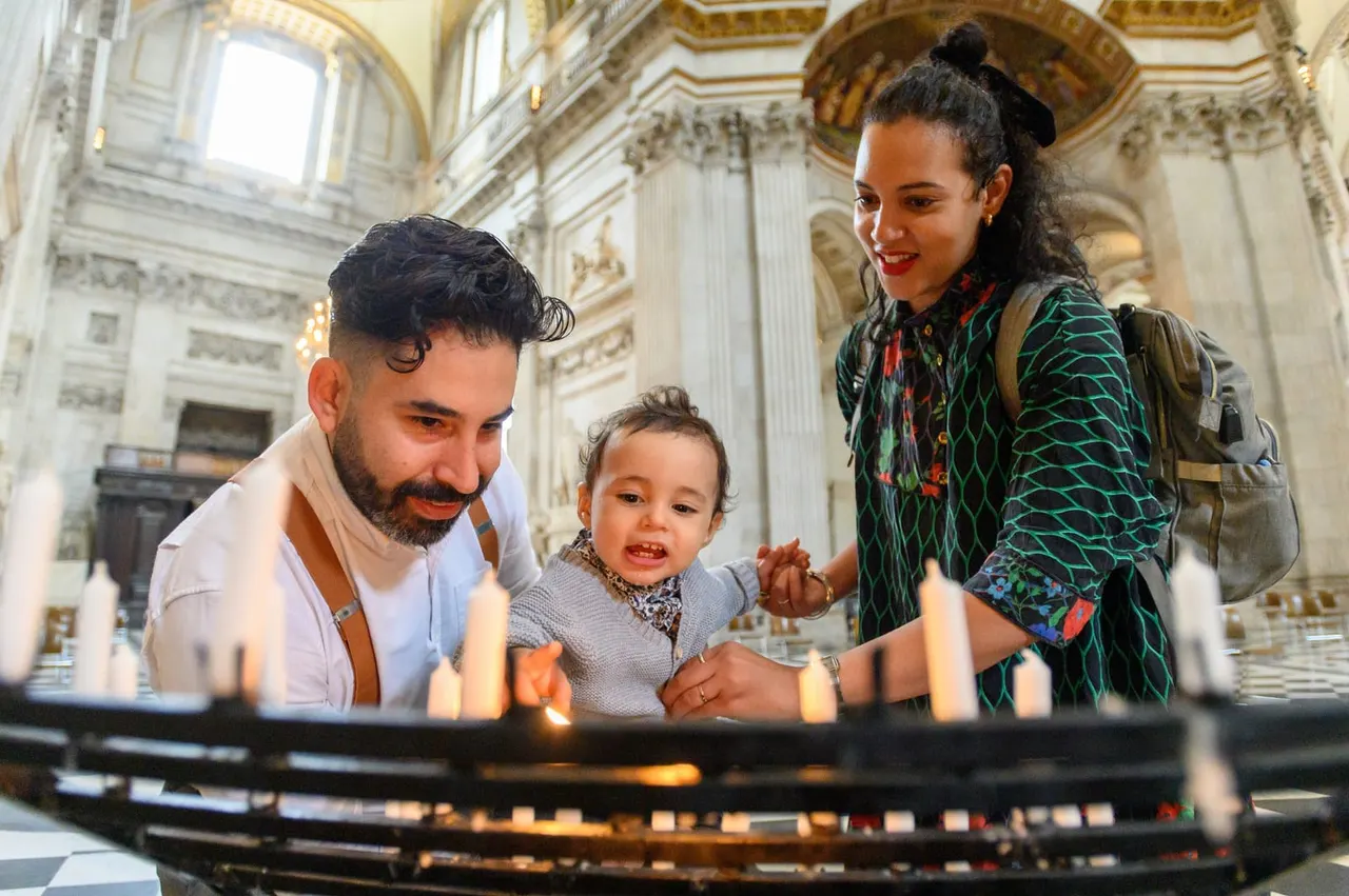 Family of three lighting candles inside an ornate cathedral with classical columns and decorative ceiling.
