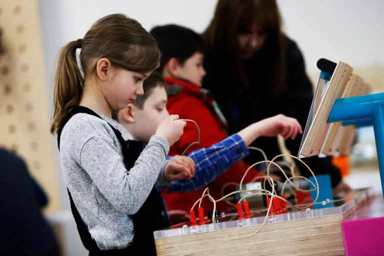 Children engaged in a hands-on science activity with wooden structures and electronic components at a learning centre.