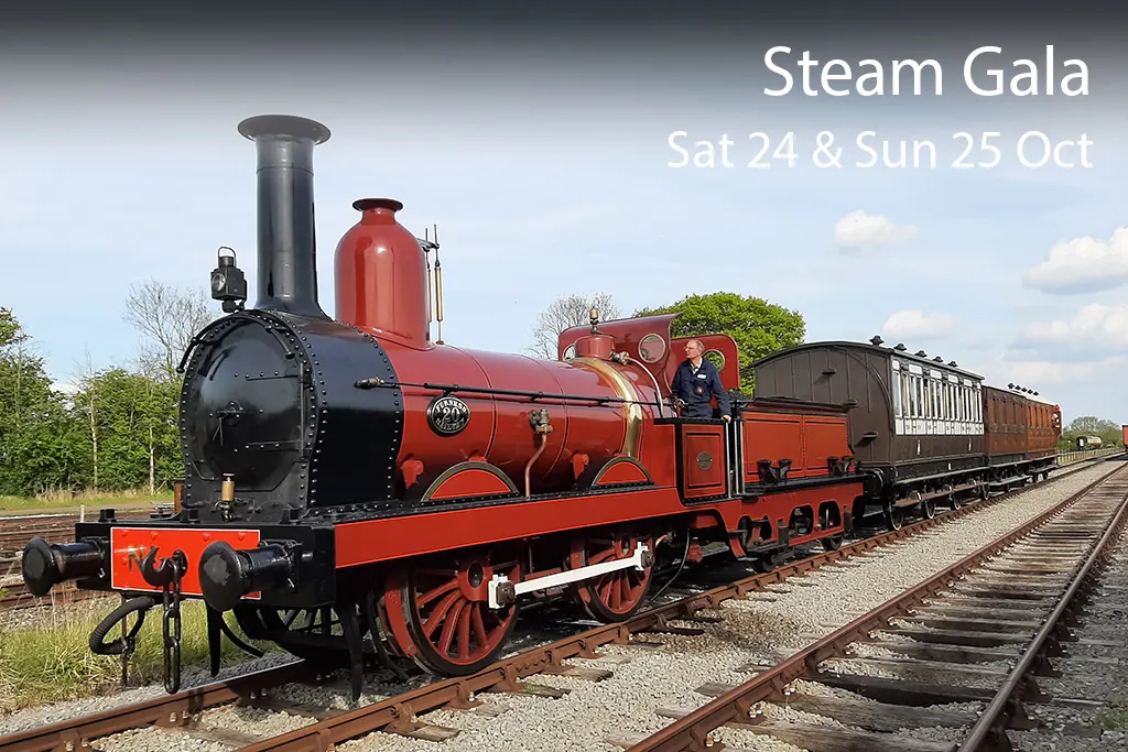 A red and black heritage steam locomotive with passenger carriages on railway tracks, with staff members visible on the engine.