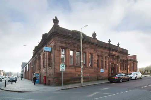 Historic red sandstone corner building with classical architecture, parked cars, and street signage on an urban street.