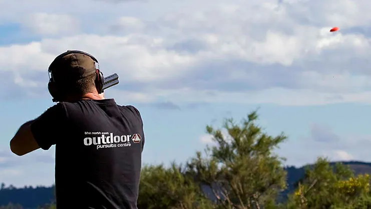 Person aiming a shotgun at a clay target in the sky during a shooting activity.