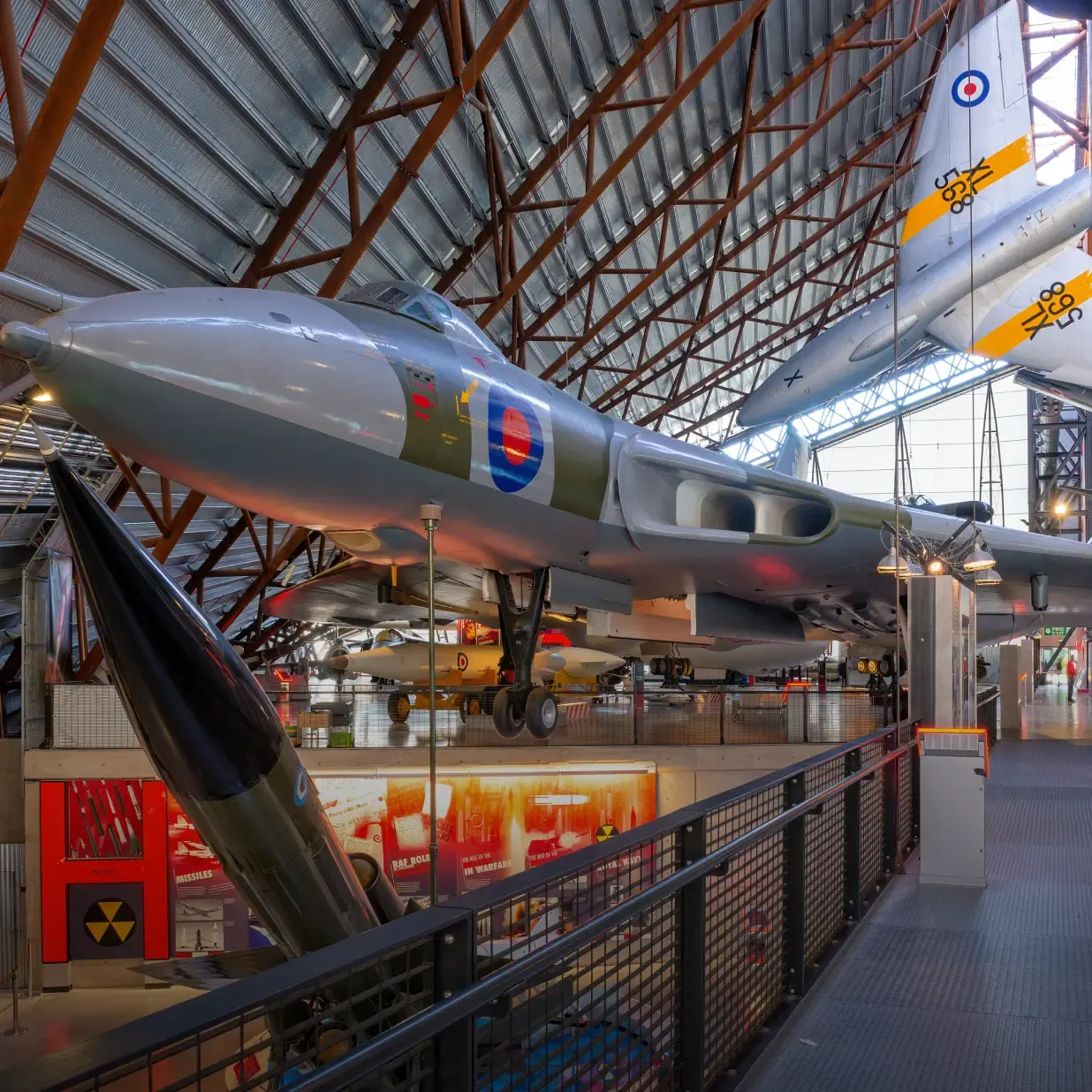 Historic military aircraft on display in a museum hangar with viewing platform and exhibition panels.