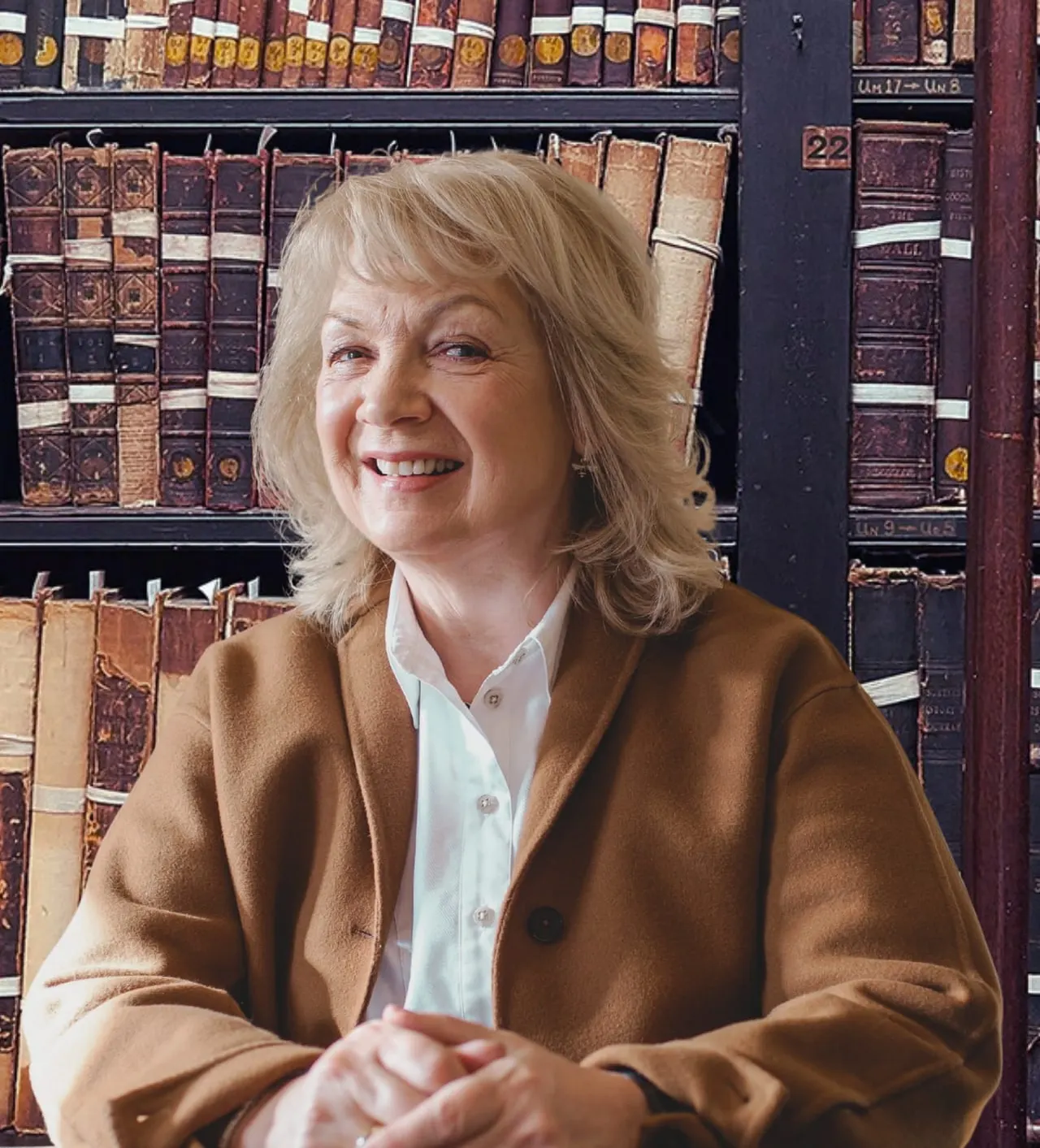 Woman smiling in front of shelves of antique leather-bound books.