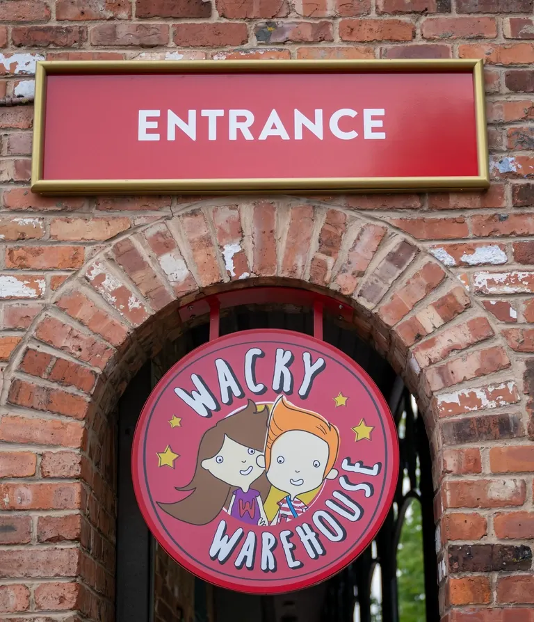 Red "Entrance" sign mounted on brick wall above archway with Wacky Warehouse logo.
