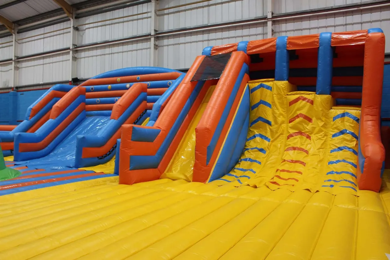 Large inflatable play structures with slides and obstacles in a warehouse-style indoor play area.
