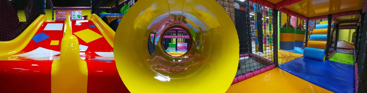 Interior of a children's play centre with colourful inflatables, slides, and a large yellow tunnel tube in the foreground.