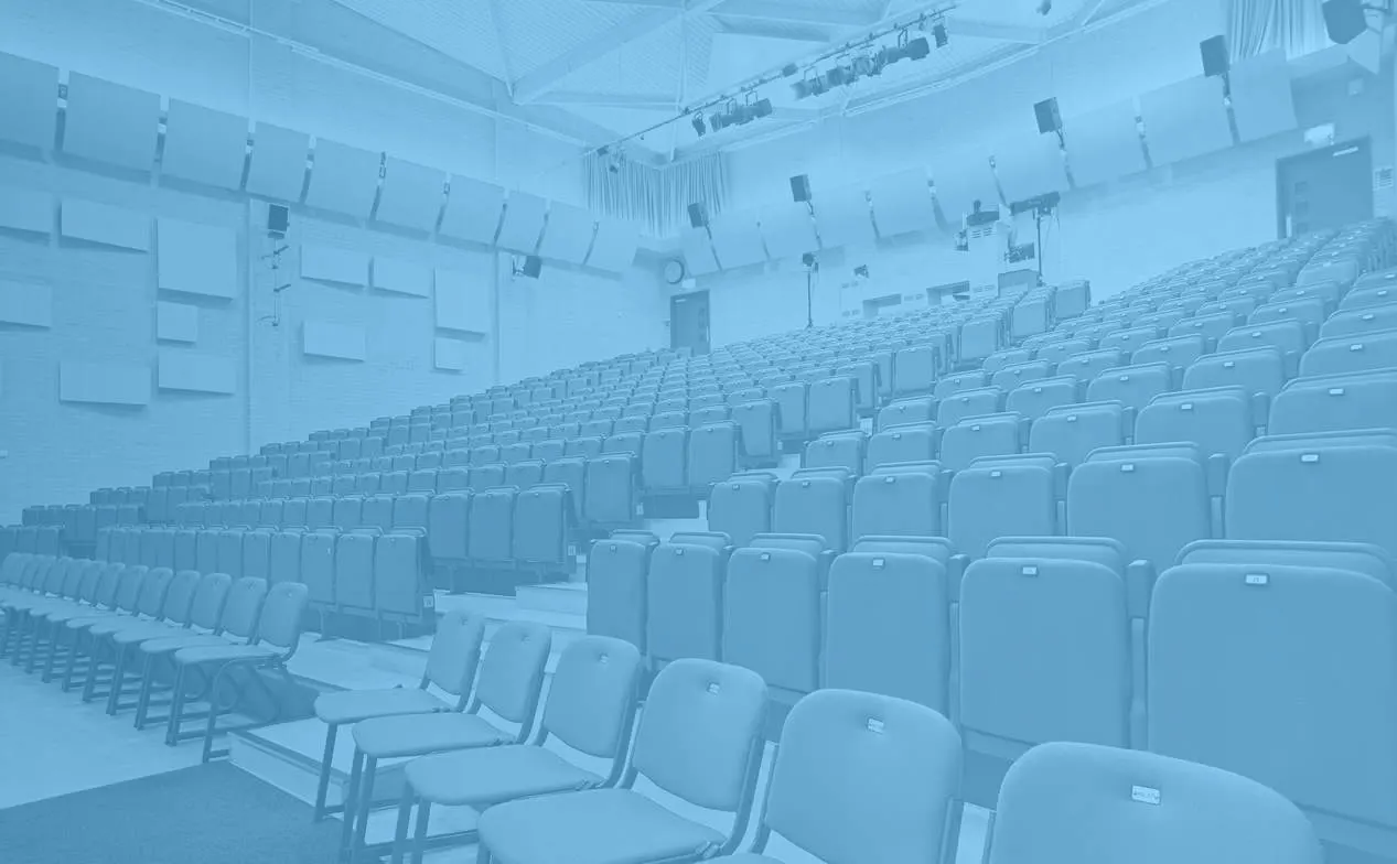 Empty cinema auditorium with rows of blue seats facing the screen, professional lighting rigs overhead.