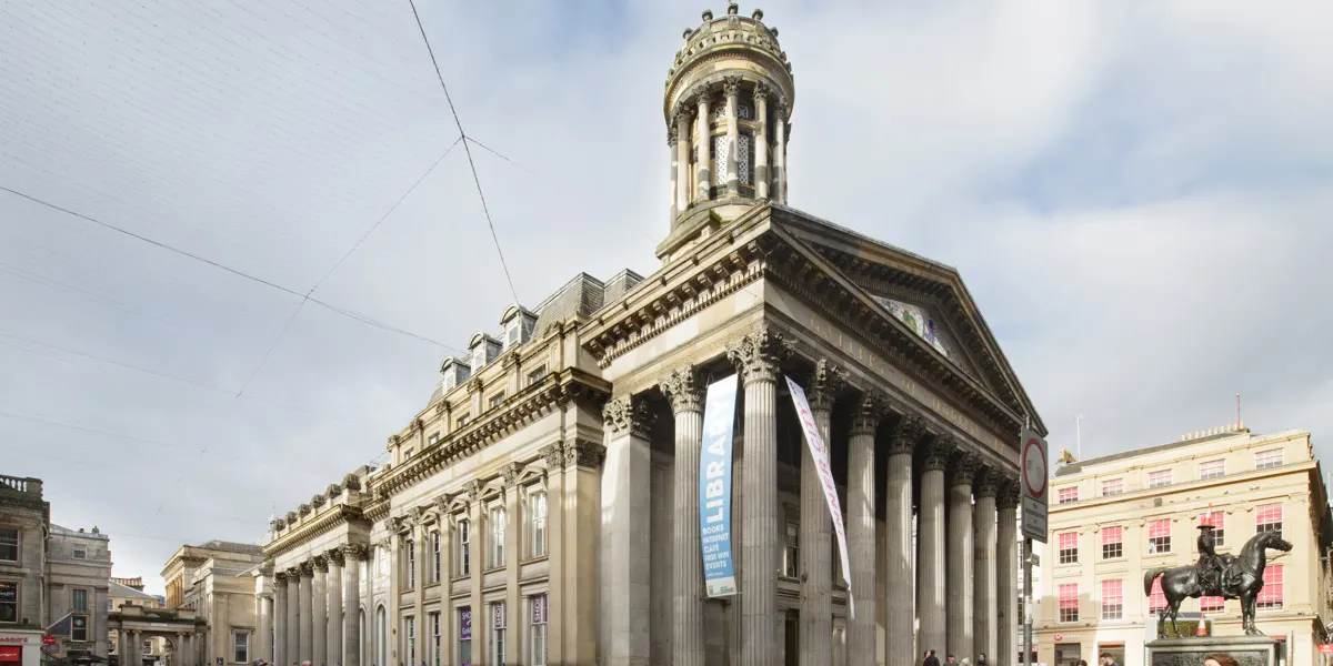A grand neoclassical stone building with tall columns and a domed tower, situated in an urban plaza alongside historic architecture.