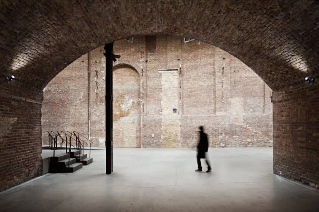 Person walking through a brick archway into a large industrial space with exposed brick walls.