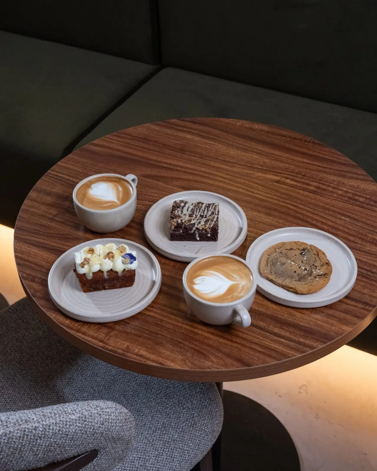 Coffee drinks with latte art and assorted pastries arranged on a wooden round table in a modern café seating area.