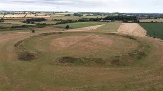 Aerial view of an ancient circular earthwork surrounded by cultivated fields and woodland.