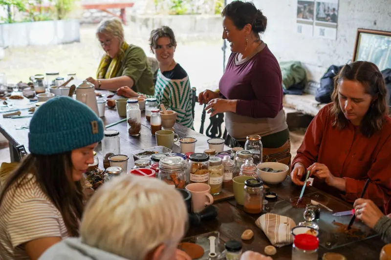 A group of people gathered around a table with jars and natural materials during a craft or workshop activity indoors.