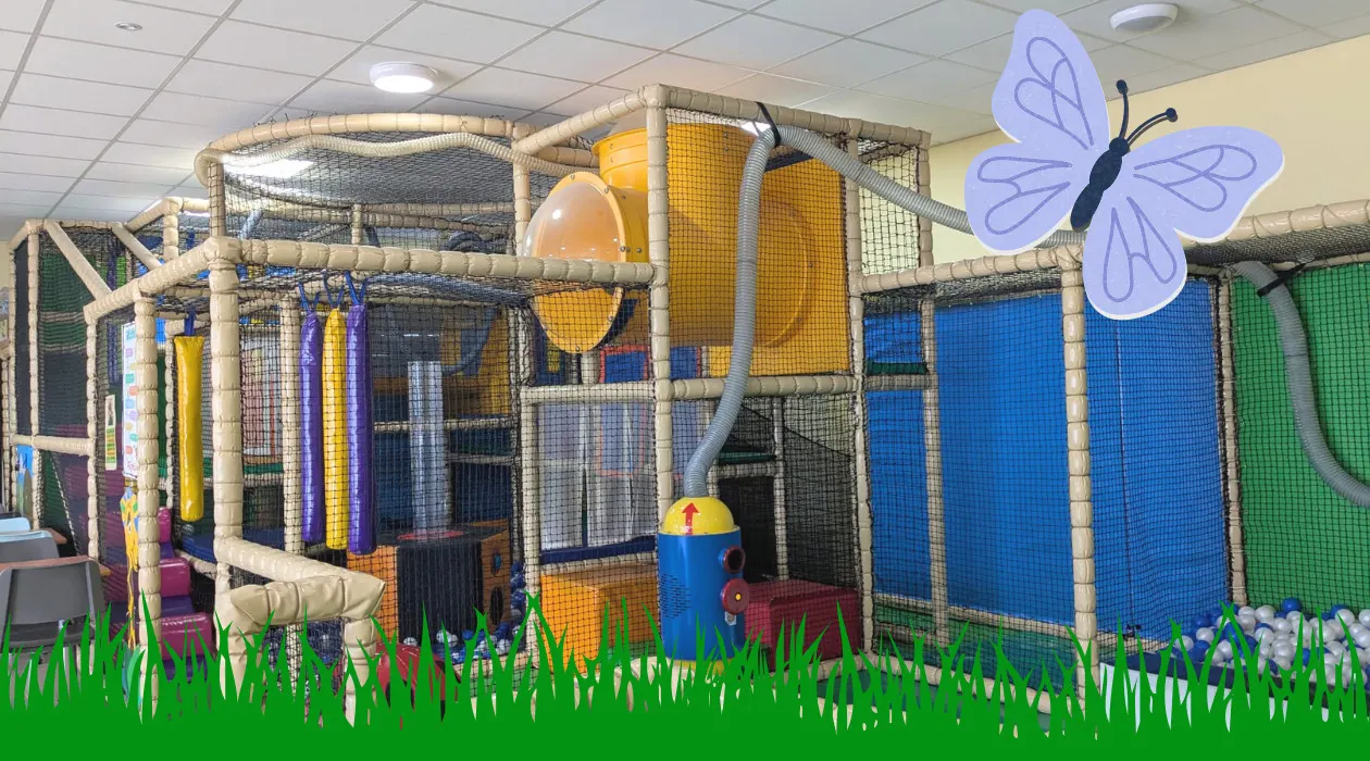 Large indoor soft play structure with tubes, slides and climbing features, decorated with butterfly and grass motifs.