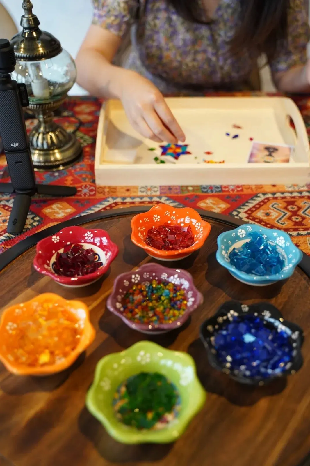 Child arranging coloured beads in small decorative bowls during a craft activity at a table.