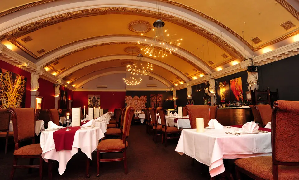 Elegant dining room with arched ceiling, pendant chandeliers, red and gold décor, and tables set for fine dining.