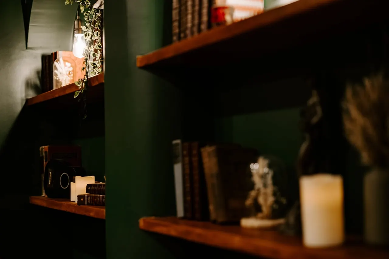 Wooden shelves on green walls displaying books, candles, and decorative items in ambient lighting.