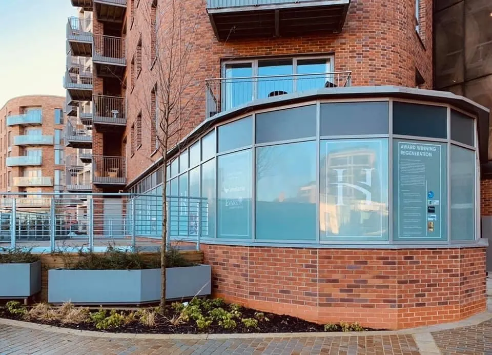 Modern curved glass frontage of a waterside café building with red brick residential apartments above.