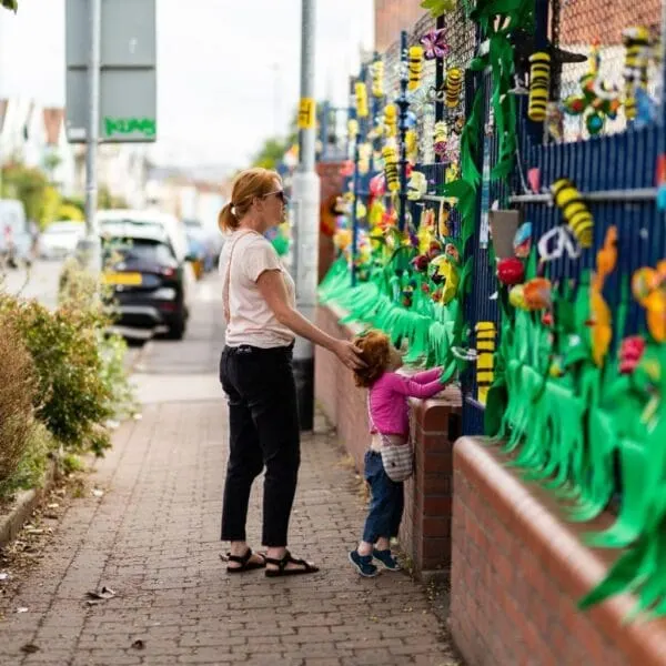 Woman and young child interacting with a colourful green wall mural decorated with bee and flower designs on an urban street.