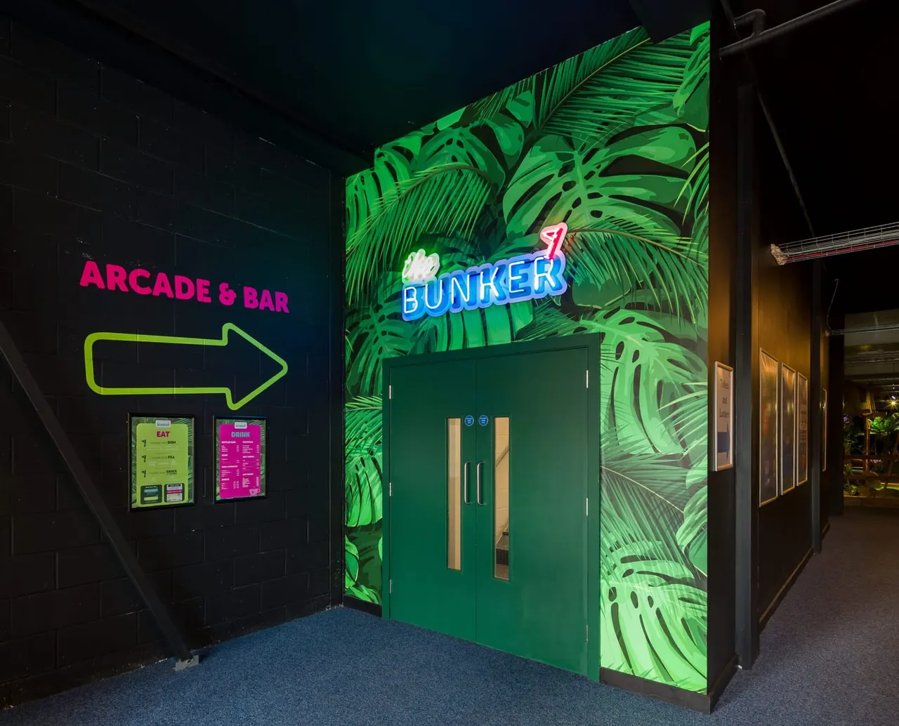 This is a designed graphic — it's a photograph of an interior venue display with overlaid neon signage and promotional graphics.

GRAPHIC