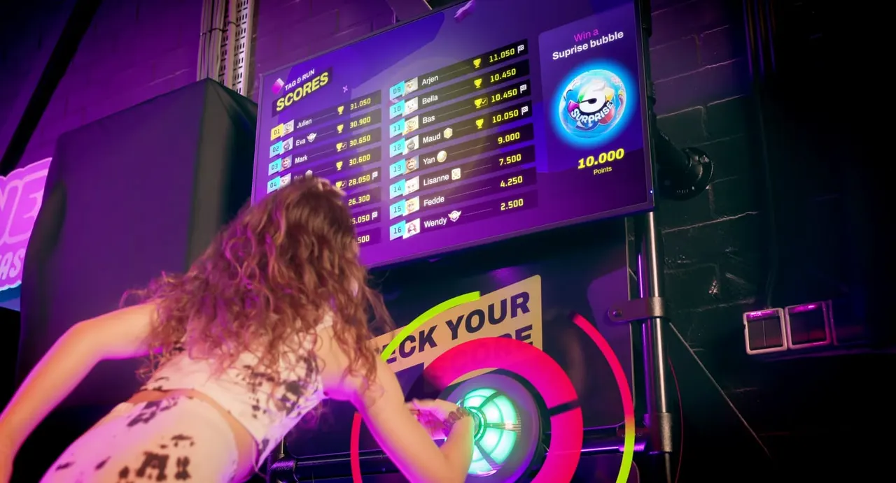 Person playing an arcade game machine lit by purple and pink neon, watching a leaderboard display above.