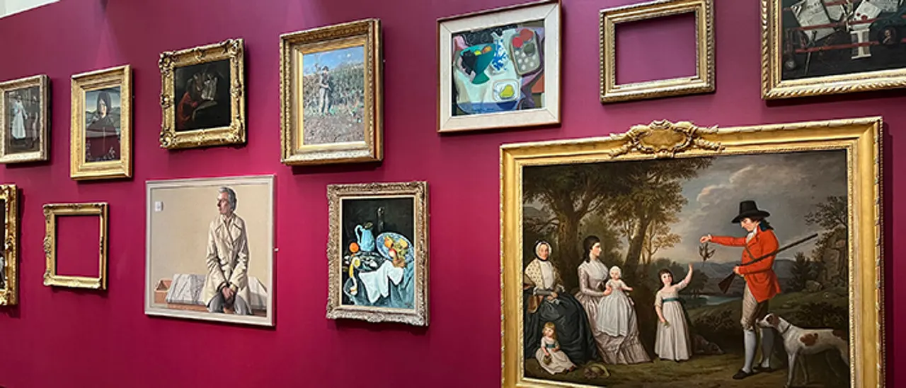 Gallery wall with multiple framed paintings and artworks hung against vibrant magenta walls, featuring ornate gold frames of varying sizes.