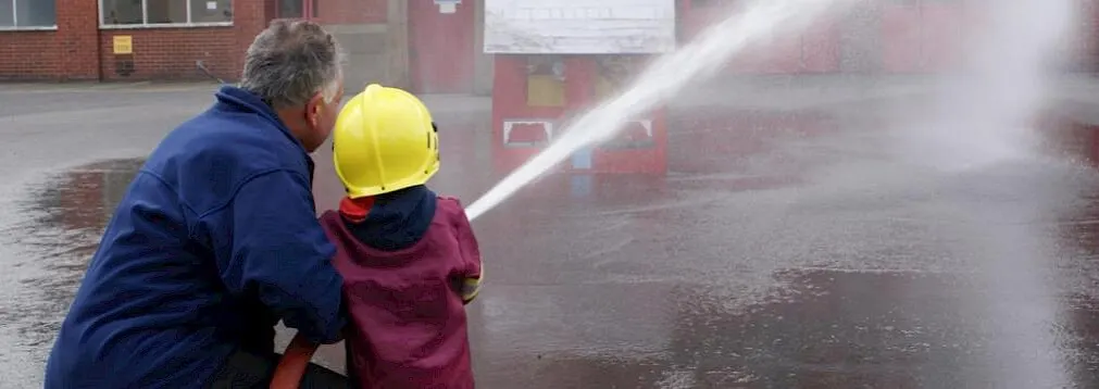 An adult and child in safety helmets operating a fire hose together on a training ground.