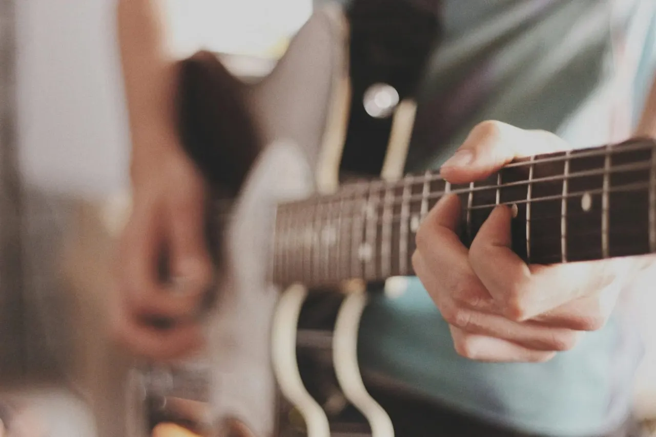 Person playing an acoustic guitar, hands positioned on the fretboard and strings.