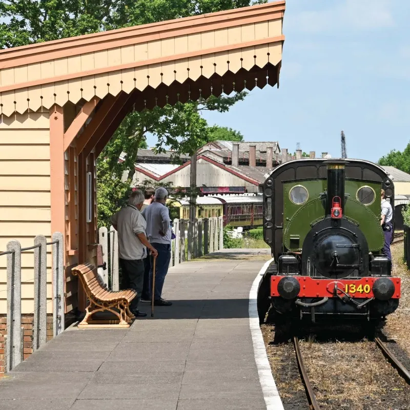 A vintage steam locomotive numbered 1340 stands at a railway platform whilst visitors wait beneath a heritage station canopy.