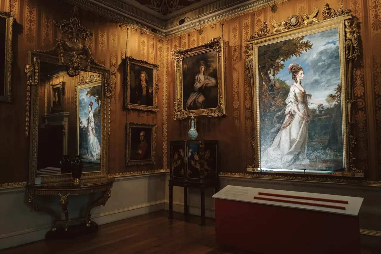Ornate period room with gilded walls displaying portraits and landscape paintings in elaborate gold frames.