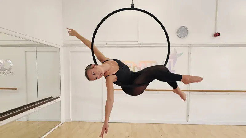 Performer suspended horizontally in a black aerial hoop during an acrobatics class.