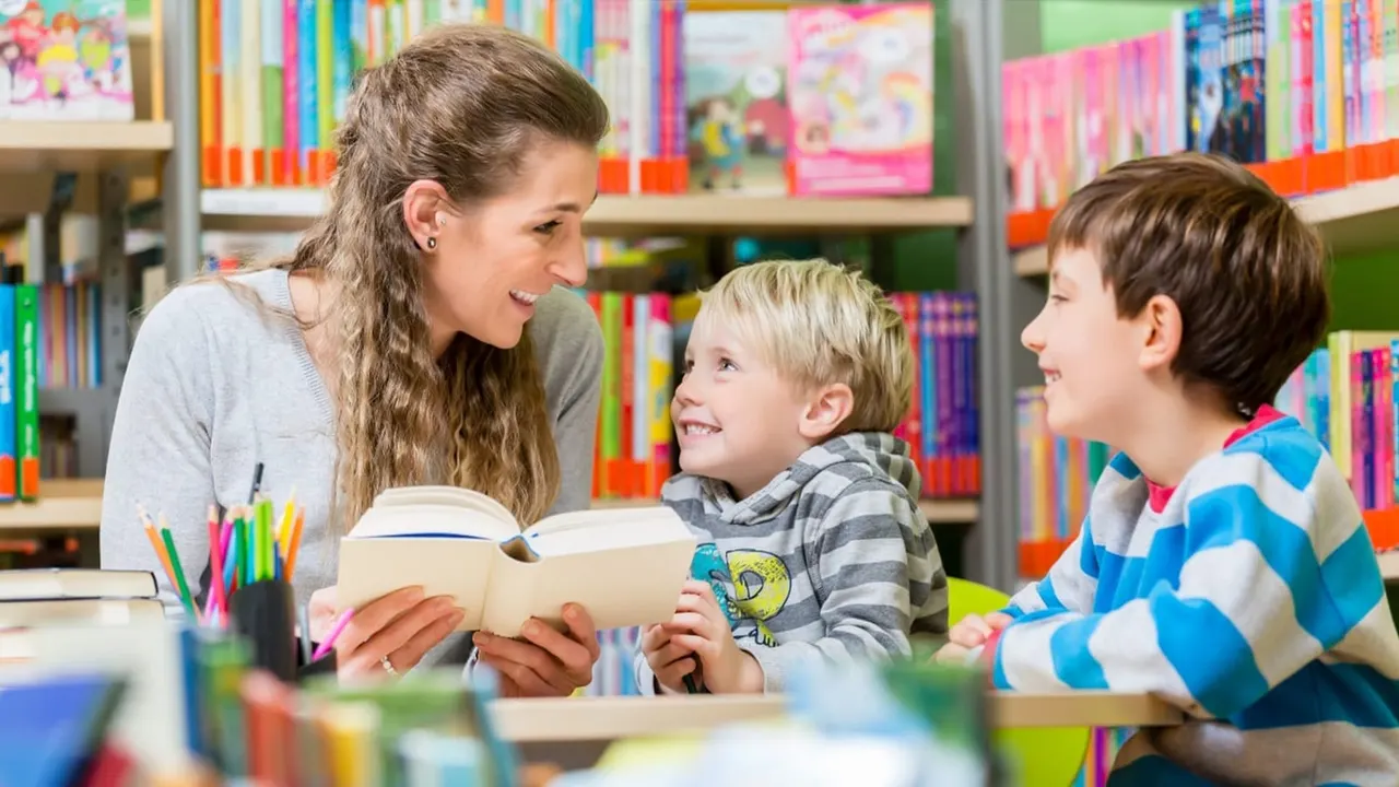 Adult reading a book with two young children in a library surrounded by colourful shelves of books.
