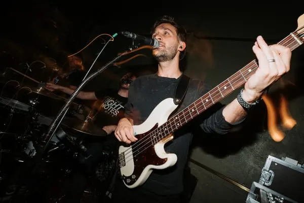 Musician performing on bass guitar and singing into microphone on stage.