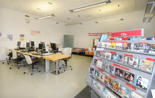 Computer workstations and shelving with CDs and media in a bright community centre room.